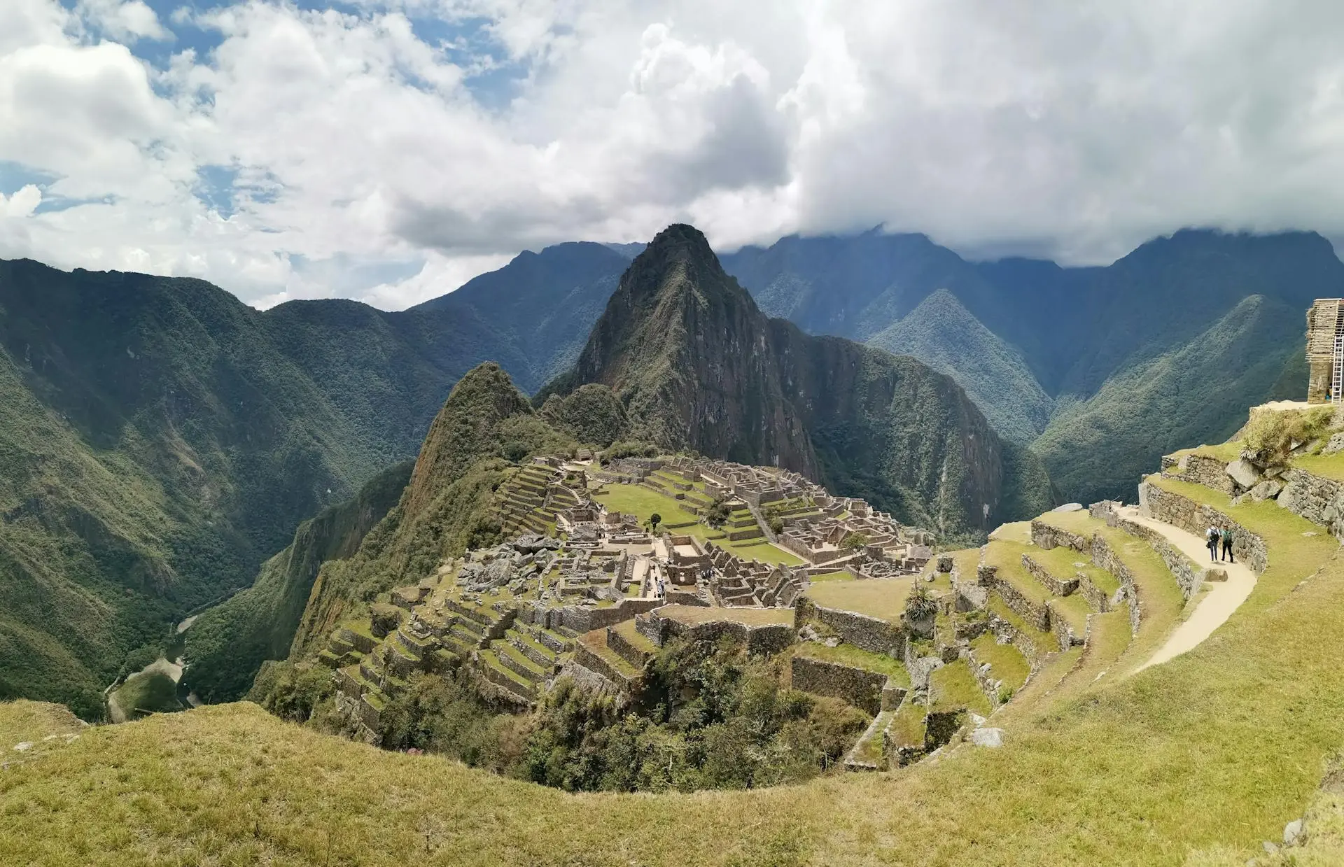 Panoramic view of the ancient Inca citadel of Machu Picchu with Huayna Picchu mountain rising behind, surrounded by lush green Andean peaks
