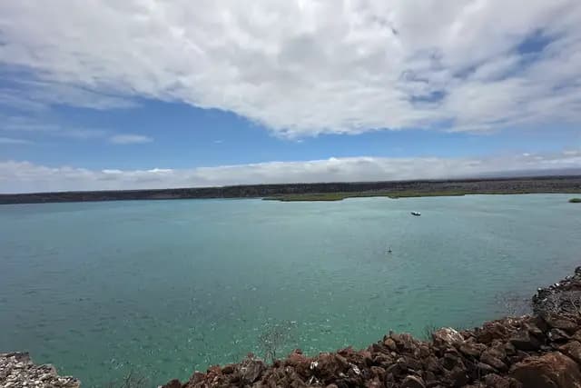 A teal lagoon behind a lava shoreline under a wide cloudy sky on Santa Cruz island, Galápagos