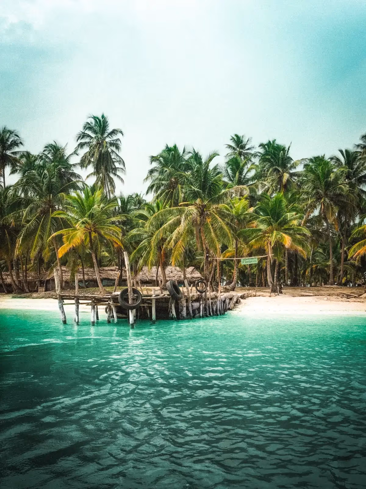 Palm-fringed beach with a wooden stilt dock on a Guna Yala island, San Blas, Panama
