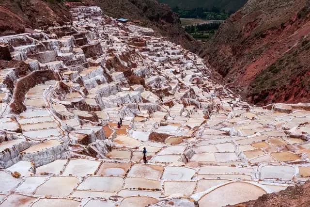 The terraced white salt pans of Maras cascading down a red-earth valley in the Sacred Valley, Peru