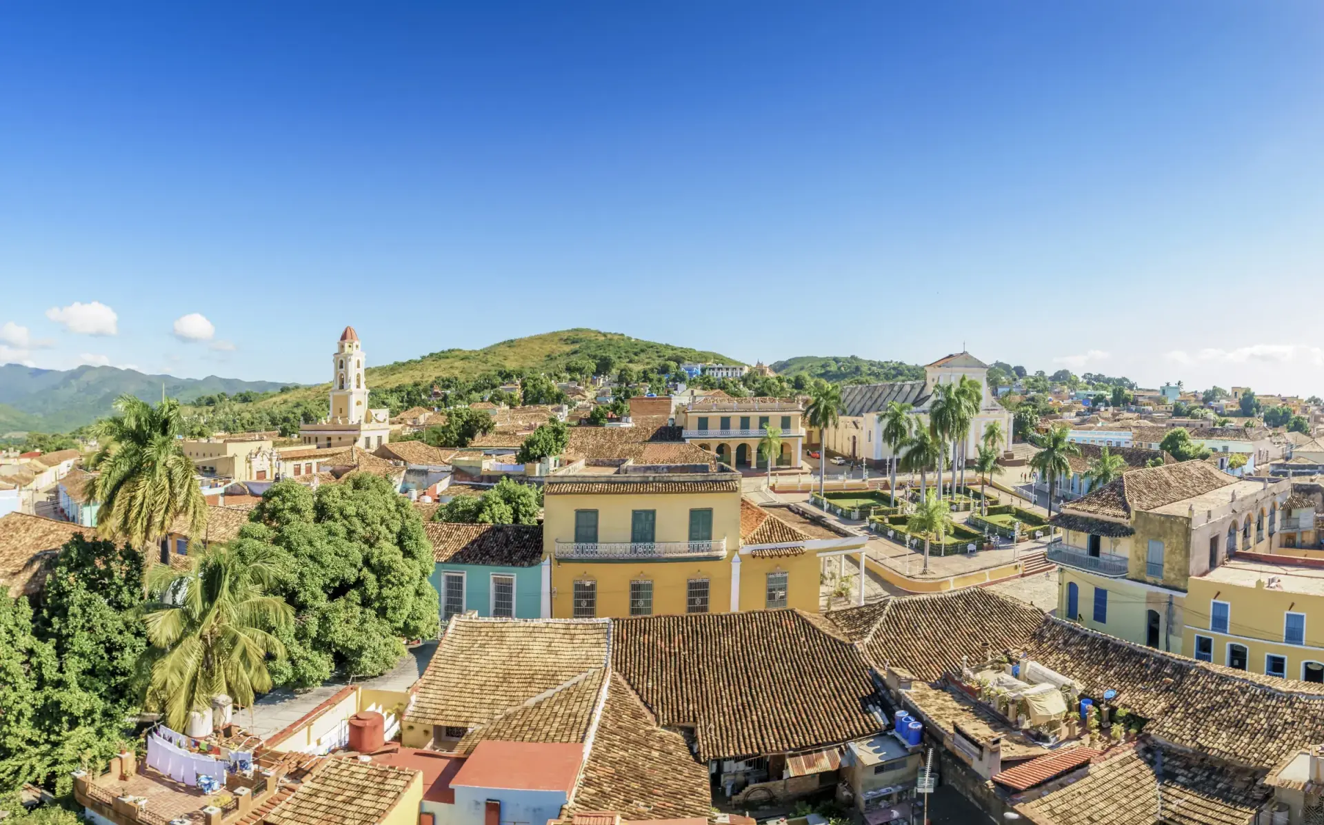 Rooftop view across Trinidad in Cuba showing terracotta tiles, colonial bell tower and the Sierra del Escambray mountains
